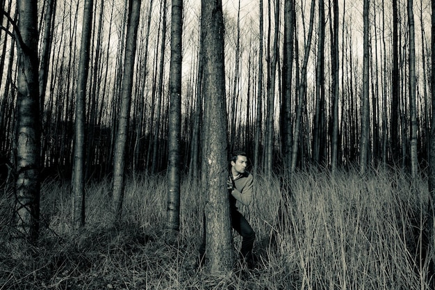 Photo alert man standing behind tree in forest against sky