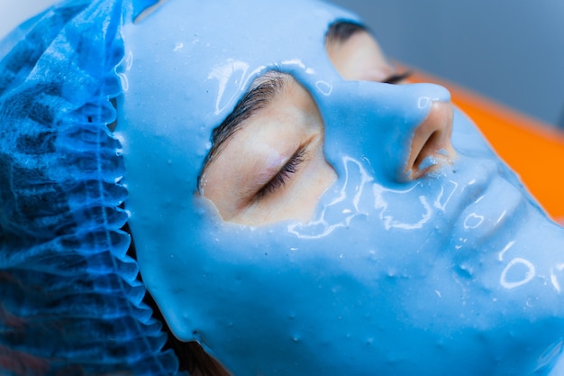 Alginaat hydraterend masker voor gezicht en huid van jonge meisjes. spa-procedure voor verjonging. schoonheidsspecialiste smeert blauw masker uit. dermatologie in de medische kliniek