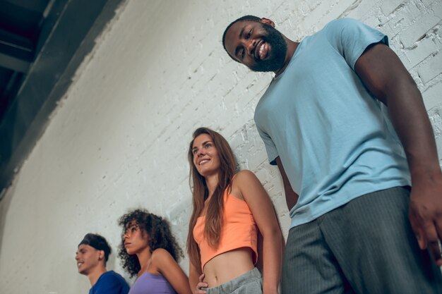 Alignment. Joyful smiling guys and girls in casual clothes standing in row near the wall 