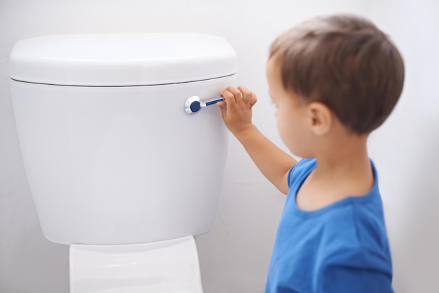 Photo all done shot of a cute young boy flushing a toilet