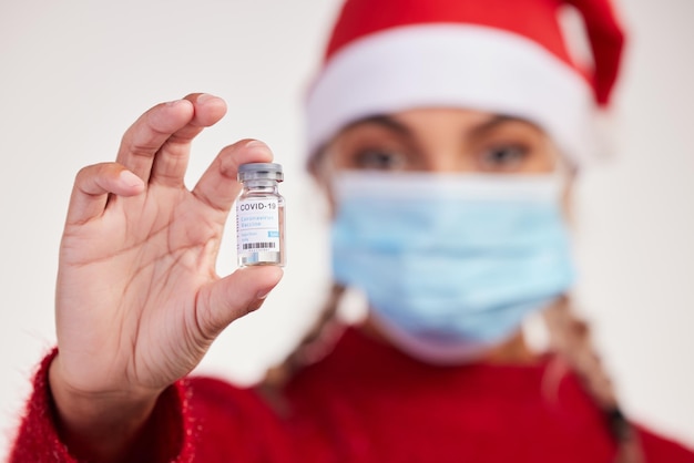 All I want for Christmas is a vaccine Studio shot of a young woman holding vaccine and wearing a mask against a grey background