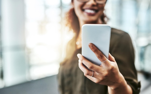 All the info she needs is in one small device Cropped shot of an unrecognizable businesswoman using a smartphone while standing in a modern office