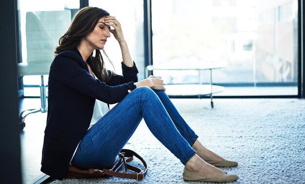 All this stress is giving her a headache Shot of a stressed businesswoman sitting on the floor outside the boardroom