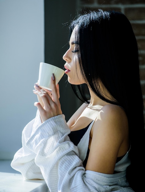 Alleen drinken Mooie vrouw die verse hete koffie drinkt bij het raam Sensueel meisje dat haar favoriete ochtenddrankje drinkt Sexy meisje met keramische drinkbeker