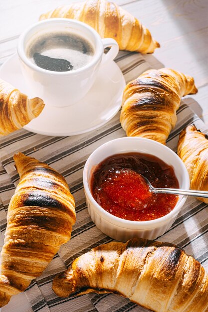 Alleen vers gebakken croissants met jam en koffie op tafel in de ochtendzon heerlijk ontbijtconcept
