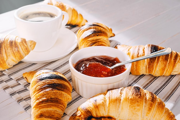 Alleen vers gebakken croissants met jam en koffie op tafel in de ochtendzon heerlijk ontbijtconcept