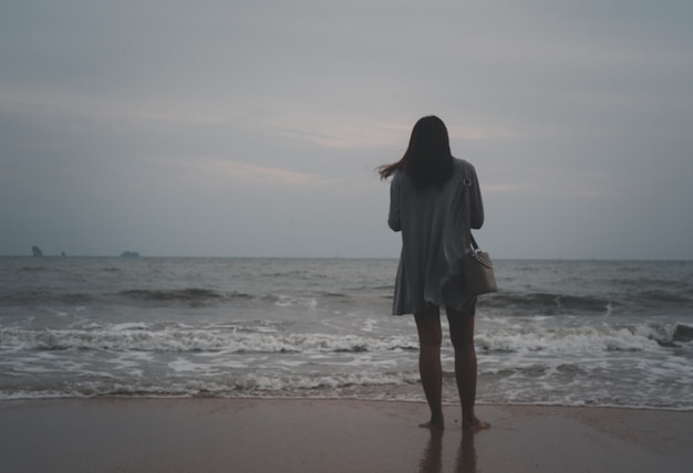 Alleenstaande vrouw die alleen loopt en reflecteert op het strandoppervlak op een stormachtige achtergrond op de zee