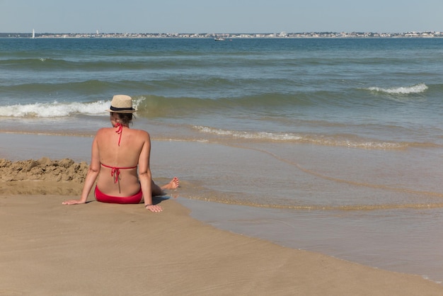 Alleenstaande vrouw zittend op het zand kijkend naar de oceaan