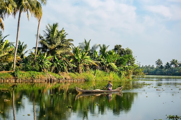 Photo alleppey alappuzha india a man driving the slick fishing boat in backwaters of kerala having lush green palm trees in background