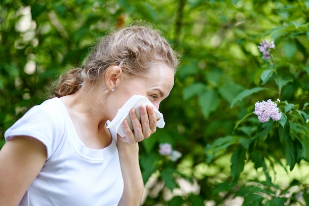 Allergie. Vrouw die haar neus blaast wanneer status dichtbij bloemen in een park. Vrouw met infectie niezen