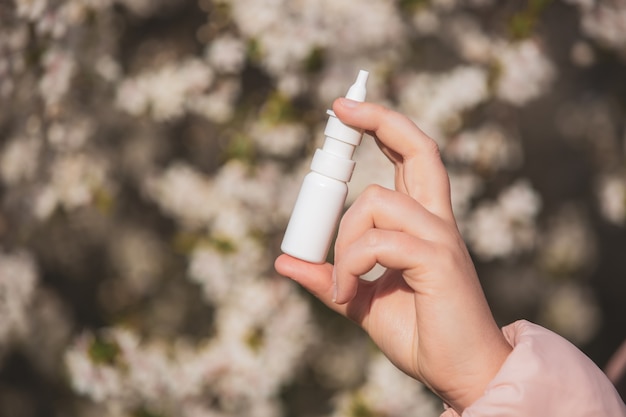 Концепция аллергии, молодая женщина с носом или назальным спреем в руке перед цветущим деревом в весенний сезон, здравоохранение