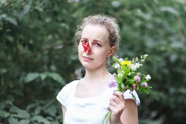 Photo allergy woman squeezed her nose with a clothespin so as not to sneeze from the pollen of flowers