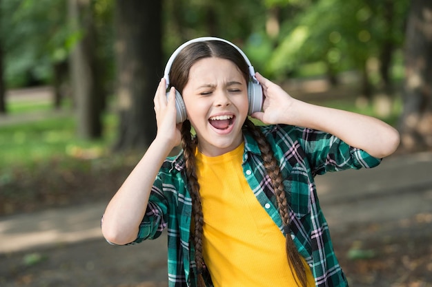 Alles behalve muziek. Gelukkig meisje zingen naar muziek zomer buitenshuis. Klein kind draagt een koptelefoon die muziek afspeelt. Modern leven. Nieuwe technologie. Zomervakantie. Vrije tijd en plezier. Geef toe aan de groove.