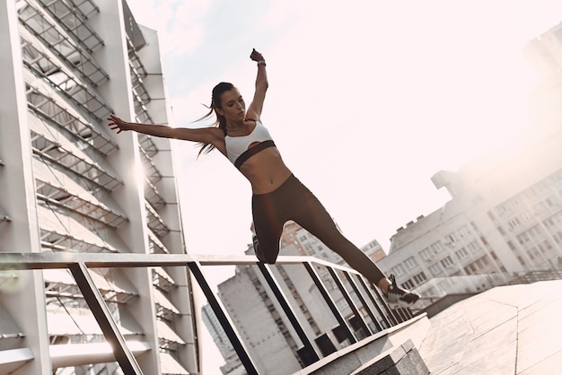 Alles is mogelijk. Volledige lengte van moderne jonge vrouw in sportkleding die springt tijdens het sporten buitenshuis