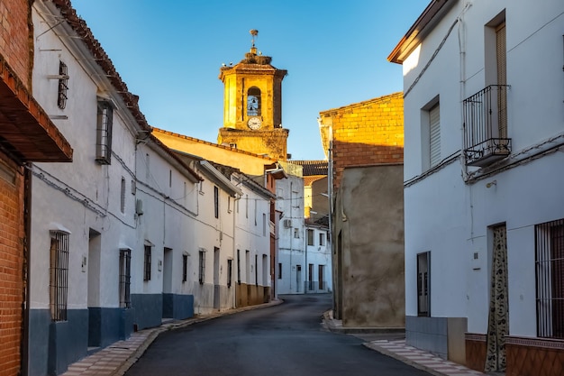 Alley with old houses painted white and tower of the catholic church illuminated by the light of daw
