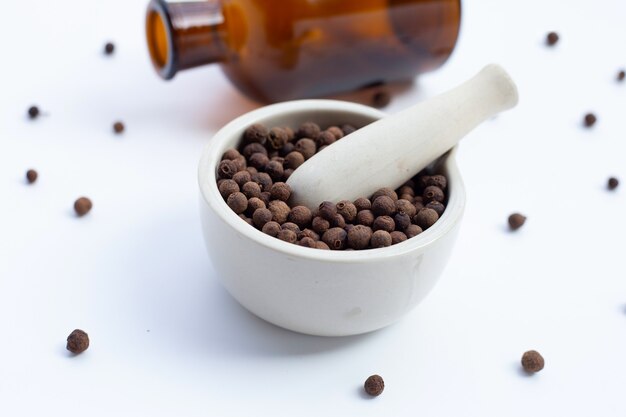 Allspice in porcelain mortar with pestle on white background.