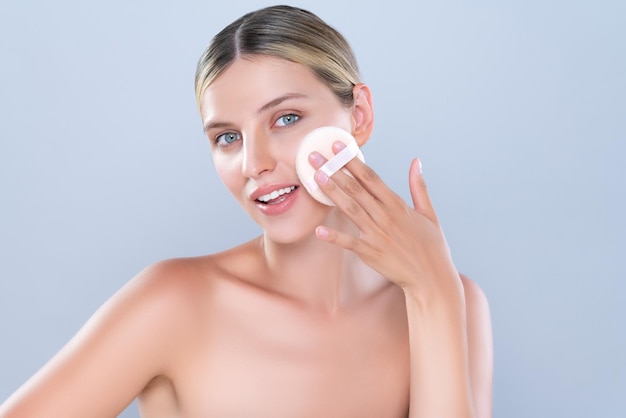 Alluring beautiful female model applying powder puff for facial makeup concept