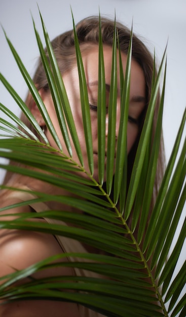 Alluring in good shape bewitching female model over 20s in sandy clothes cuddling the fern leave during the shooting process