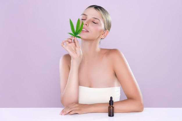 Alluring portrait of beautiful woman holding green leaf with CBD oil bottle