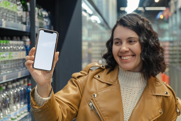 An alluring woman grips a whitescreened phone in a grocery store