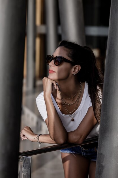 Alluring woman in sunglasses resting while leaning on street handrail