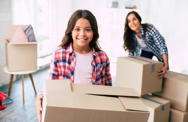 Alluring young woman and her child are holding cardboard boxes in their new house after the relocation