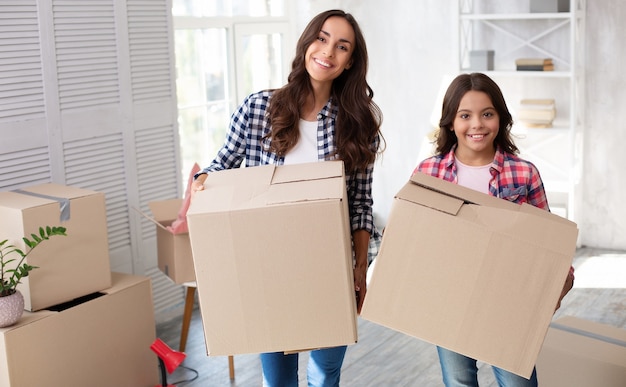 매혹적인 젊은 여성과 그녀의 아이가 이사 후 새 집에서 판지 상자를 들고 있다