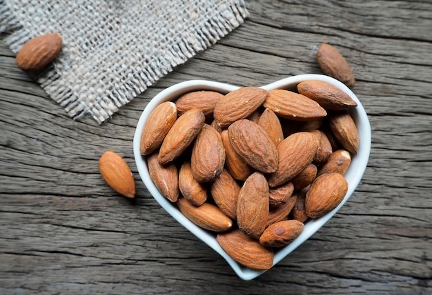 Almond in bowl shape heart on wooden background