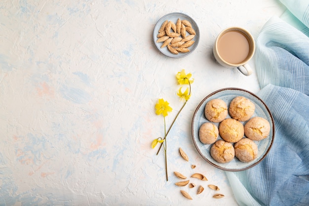 Biscotti alle mandorle e una tazza di caffè su una superficie di cemento bianco e tessuto di lino blu