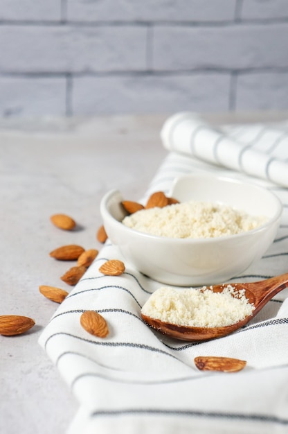 Almond flour in a bowl and spoon with scattered nuts on a white concrete background