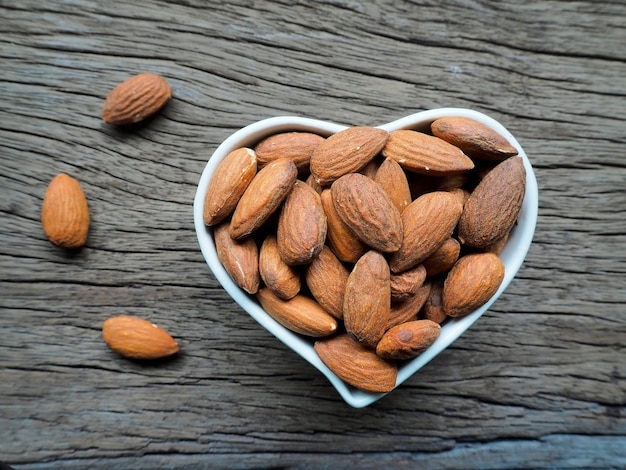 Almond in heart shape bowl on wooden back