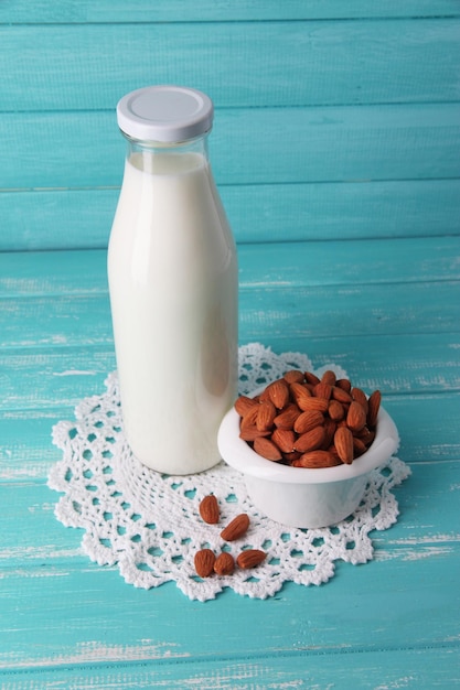Almond milk in bottle with almonds in bowl on color wooden background