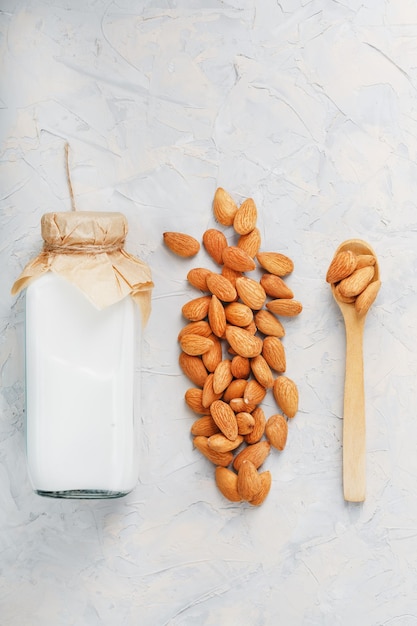 Almond milk in a bottle with a handful of seeds and a wooden spoon on a light background. Top view