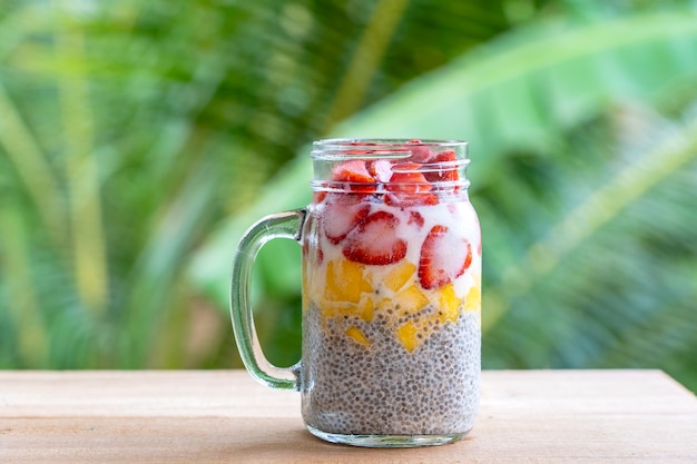 Almond milk chia pudding with fresh strawberries and mango in a glass jar mug. Vegan raw breakfast. Chia seeds and fresh cut fruits and berries dessert, close up