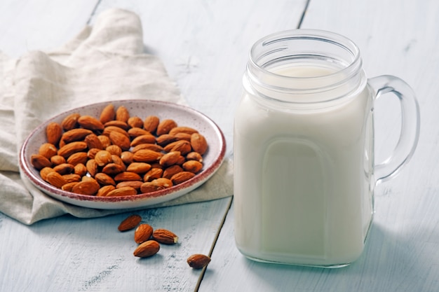 Almond milk cocktail in jar with almond nuts on rustic blue wooden table. Vegan alternative food, non-dairy milk, clean eating concept.