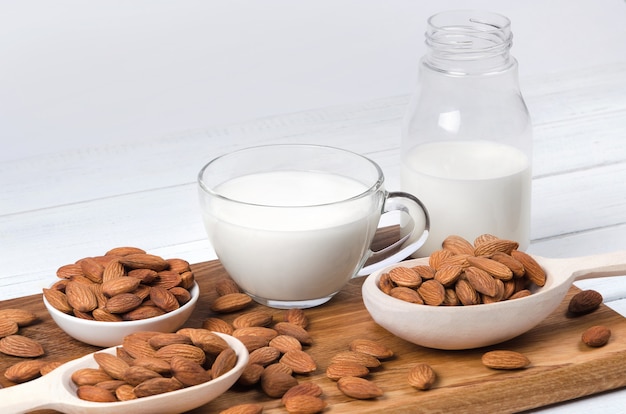 Almond milk in cup and bottle with nuts on white surface