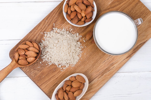 Almond milk in cup with almond flour and nuts on wooden plate