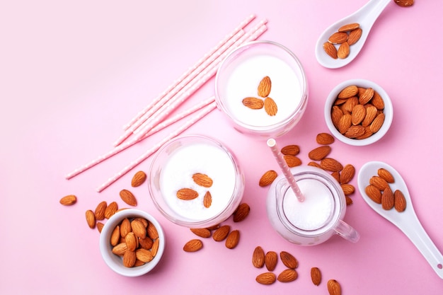 Almond milk in a decanter, two glasses and nuts on a pink background. Flat lay style