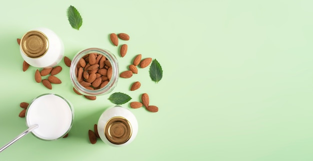 Almond milk in a glass and bottles on a light green surface