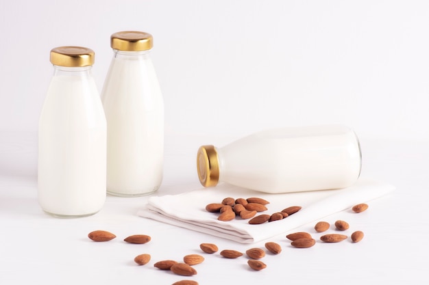 Almond milk in glass bottles stands on a white, next to the almond.