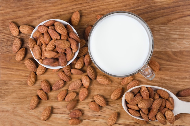 almond milk in glass with seeds and wooden spoon on wooden table