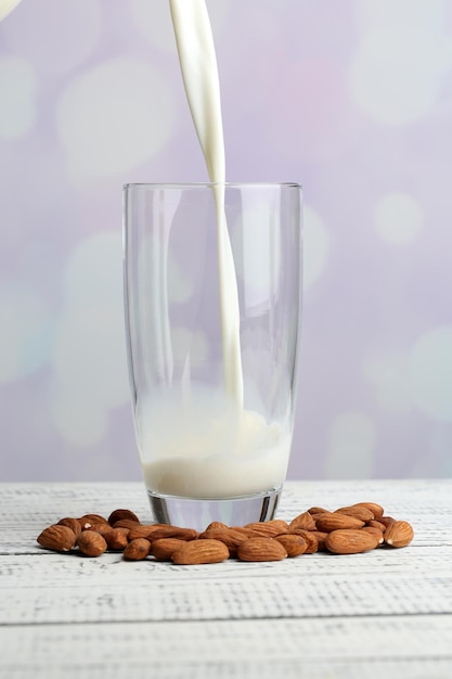 Almond milk is poured into glass on color wooden table on light background