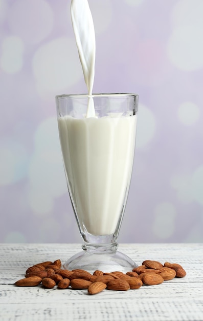 Almond milk is poured into glass on color wooden table on light background