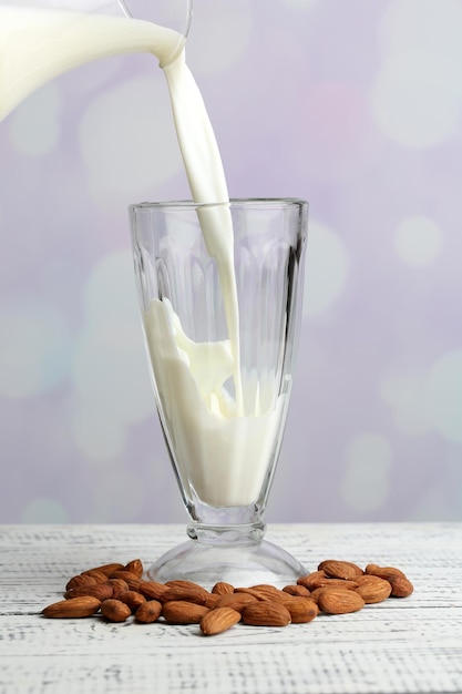 Almond milk is poured into glass on color wooden table on light background