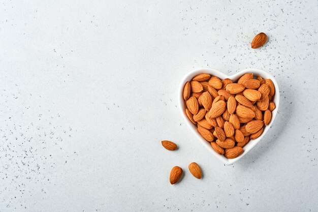 Almond nut in a heartshaped ceramic plate on white background. Snack vegan sugarfree food.