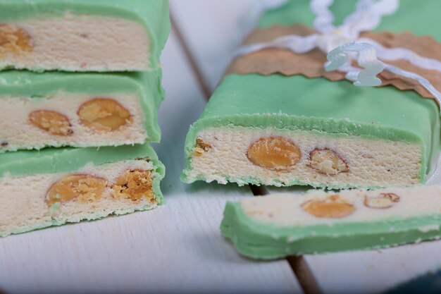 Almond turron covered by pistachio chocolate on a wooden surface. Closeup