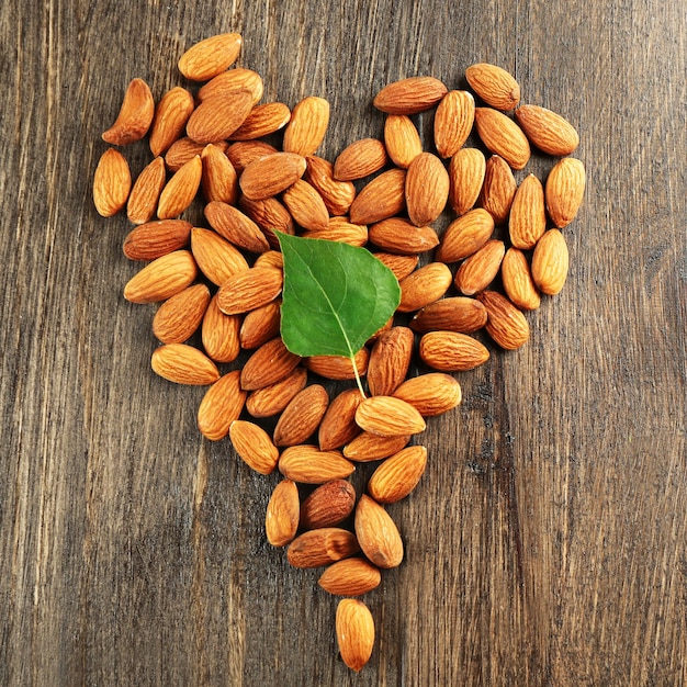 Almonds arranged in heart shape with green leaf on wooden background