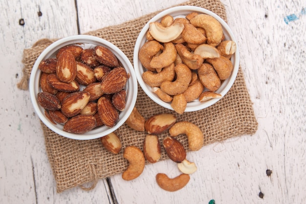 Almonds and cashew nut in the white cup and put on sack cloth on wood floor 