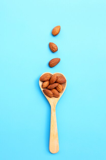 Almonds on heart shape wooden spoon on blue background.