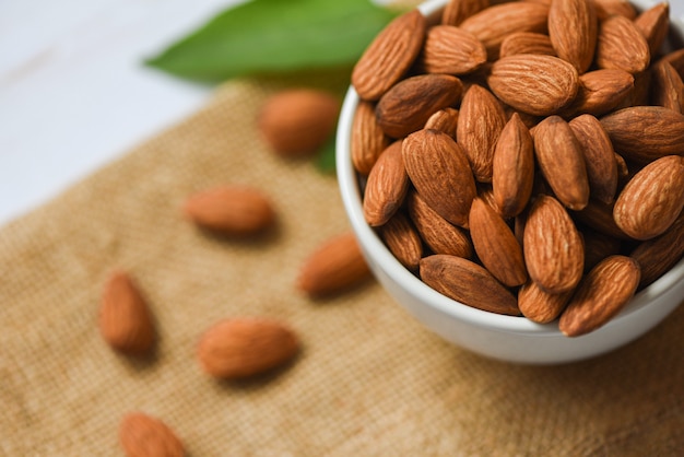 Almonds nuts on bowl with leaf top view on sack background. Roasted almond for snack